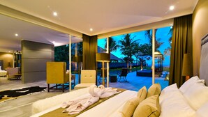 Habitación de hotel con una cama grande, un área de descanso con una silla y una mesa, vistas al exterior y un balcón con vista a palmeras.