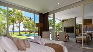 Un dormitorio amplio con una cama grande, televisor y vista a una piscina y palmeras.