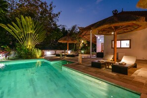 A poolside area with a clear pool, lounge chairs, and a thatched-roof structure. - Villa Udara (Sukasada)