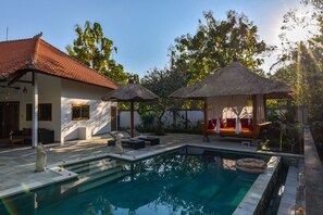 A pool area with a thatched-roof gazebo, a lounge chair, and a small statue. - Villa Udara (Sukasada)
