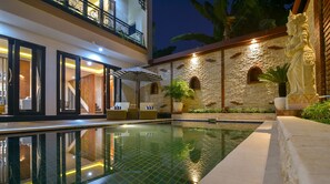 A modern pool area with a glass floor, outdoor seating, and a stone wall with a statue. - Villa Mozart (Buleleng)