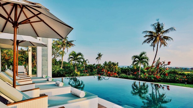 A poolside area with lounge chairs, a canopy, and a view of palm trees and a body of water. - Villa Zoubi Bali (Seririt)