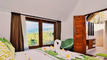 Habitación de hotel con una cama, una silla verde, una puerta de madera y vistas a un paisaje a través de amplios ventanales.