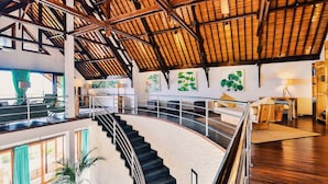 A spacious interior with a high ceiling, a staircase leading to an upper level, and artwork on the walls. - Villa Sentosa (Sukasada)