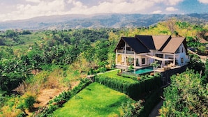 A two-story house with a large balcony, surrounded by lush greenery and a swimming pool. - Villa Sentosa (Sukasada)