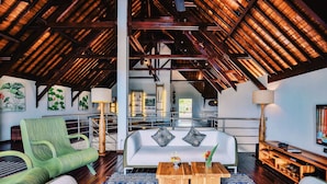 A spacious living area with a high ceiling, a sofa with cushions, a coffee table, and a television. - Villa Sentosa (Sukasada)