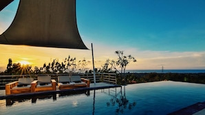A poolside area with lounge chairs and a view of the sunset over the ocean. - Villa Sentosa (Sukasada)