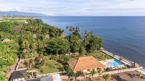 A coastal property with a swimming pool, lush greenery, and a view of the ocean. - Villa Duyung (Seririt)