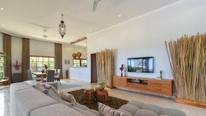A spacious living room with a large sofa, a TV, and a dining area with a table and chairs. - Villa Duyung (Seririt)