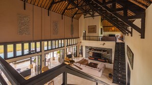 A spacious interior with a high ceiling, large windows, a fireplace, and a staircase. - Villa Bali Il Mare (Gerokgak)