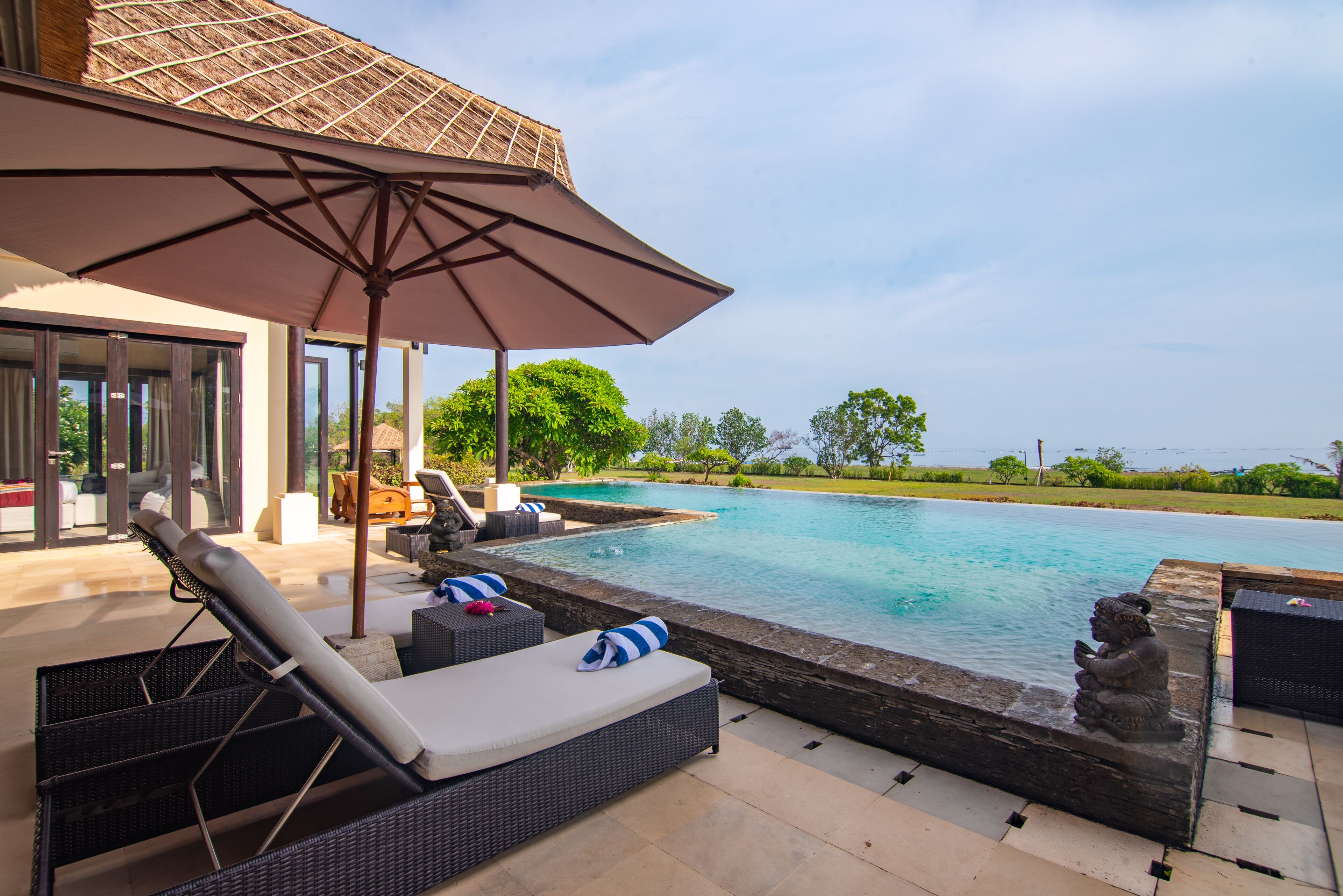 Zona junto a la piscina con sillones, una sombrilla y una estatua.