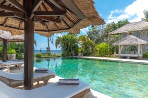 A clear blue pool with lounge chairs and a thatched-roof gazebo. - Villa Lotus (Buleleng)