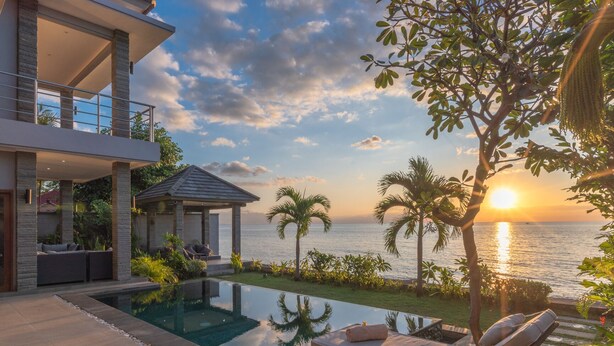 Une maison moderne avec une piscine, des chaises longues et une vue sur la mer au coucher du soleil.