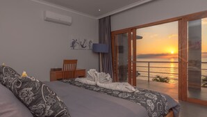 Une chambre avec un lit, une chaise, une télévision et une vue sur le coucher de soleil sur l’eau.