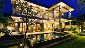 Une maison moderne à deux étages, dotée d’une piscine, de grandes fenêtres et d’un balcon.