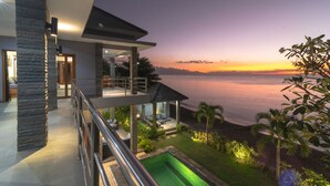 Une maison moderne dotée d’un balcon donnant sur une étendue d’eau au coucher du soleil.
