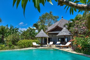 A poolside area with lounge chairs and a thatched-roof structure. - Villa Lumba-lumba 1 (Seririt)