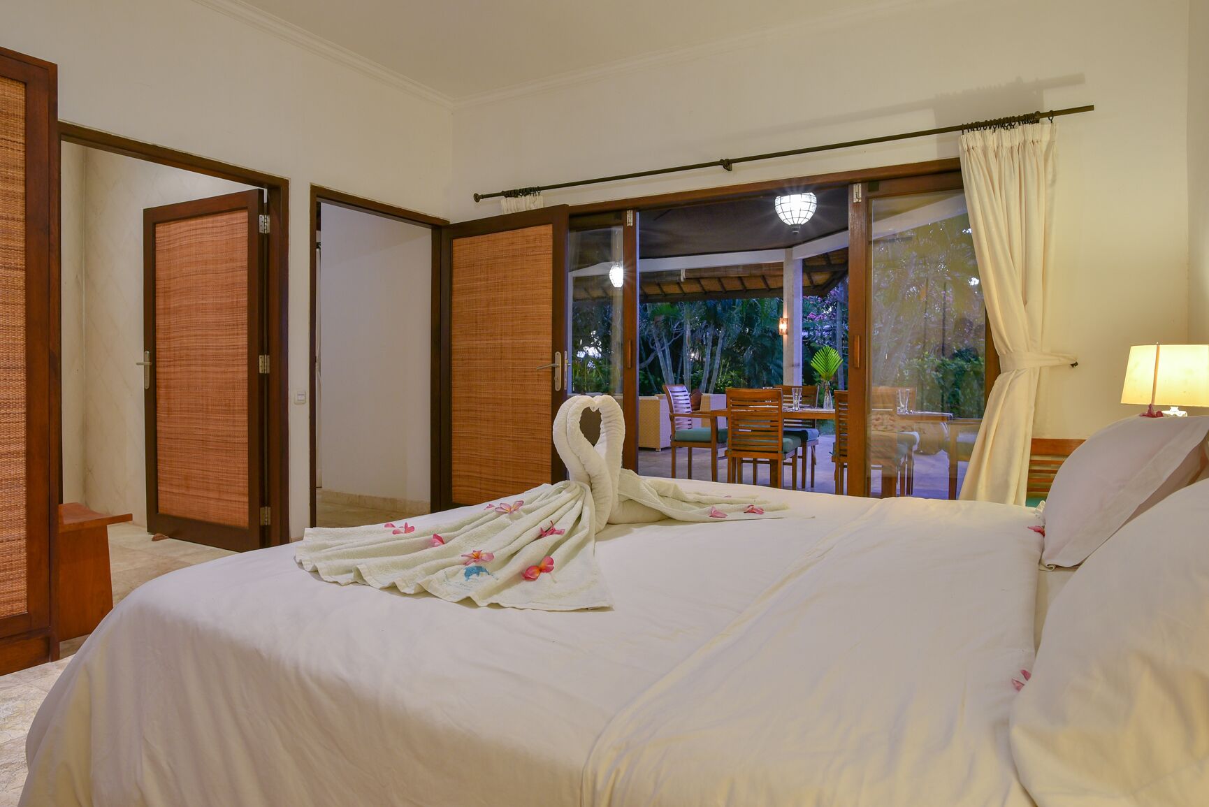 A hotel room with a bed, a view of an outdoor seating area, and a sliding glass door.