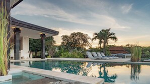 A modern pool area with lounge chairs, a stone sculpture, and a covered seating area. - Villa Pondok Wahyu Sedana (Seririt)