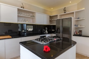 A modern kitchen with a central island, stainless steel appliances, and white cabinetry. - Villa Pondok Wahyu Sedana (Seririt)
