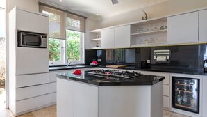 A modern kitchen with a central island, built-in microwave, and a wine fridge. - Villa Pondok Wahyu Sedana (Seririt)