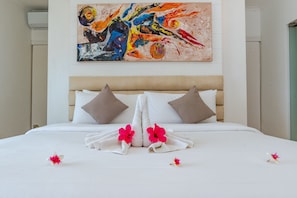 A neatly made bed with white linens, two pillows, and a floral arrangement. - Villa Pondok Wahyu Sedana (Seririt)