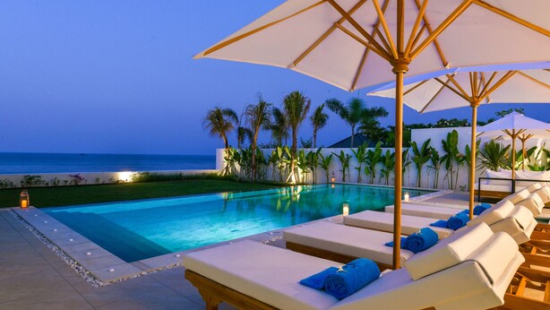 A poolside area with lounge chairs and umbrellas, a clear view of the ocean, and a well-maintained pool. - Villa Serenity (Buleleng)
