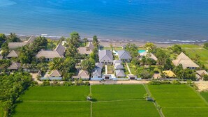 An aerial view of a coastal residential area with houses, green fields, and a beach. - Villa Serenity (Buleleng)