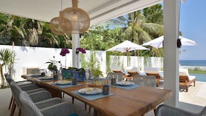 A dining area with a wooden table, wicker chairs, and white umbrellas. - Villa Serenity (Buleleng)