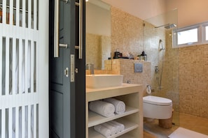 A modern bathroom with a large mirror, a white sink, a toilet, and a shower area. - Villa Serenity (Buleleng)