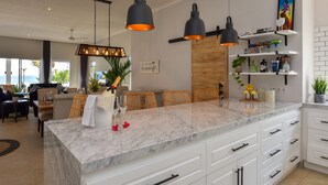 A modern kitchen with a marble countertop, white cabinetry, and pendant lighting. - Villa Serenity (Buleleng)