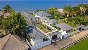 A coastal residential area with houses featuring sloped roofs and white walls, surrounded by lush greenery and palm trees, with the ocean in the background. - Villa Serenity (Buleleng)
