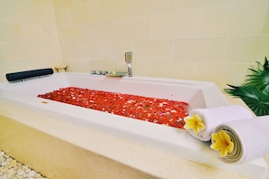 A bathtub filled with red pebbles, a black bath mat, a white towel with yellow flowers, and a small plant beside it. - Villa Banyan (Seririt)