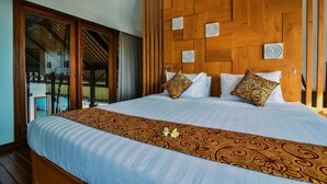 A large bed with a patterned bedspread, a wooden headboard with circular designs, and a view of a pool through a glass door. - Villa Banyan (Seririt)