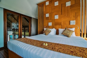 A large bed with a patterned bedspread, a wooden headboard with circular designs, and a view of a pool through a glass door. - Villa Banyan (Seririt)