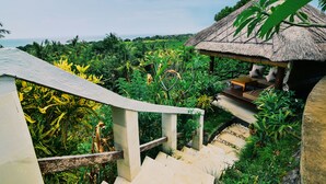 A staircase leading to a thatched-roof structure surrounded by lush greenery and a view of the ocean. - Villa Banyan (Seririt)