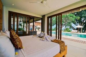 A large bed with a wooden headboard, a ceiling fan, and a view of a swimming pool.