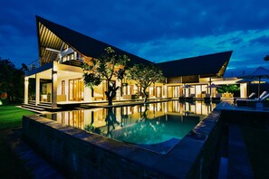 A modern house with a swimming pool, a covered patio, and a well-lit exterior at night.