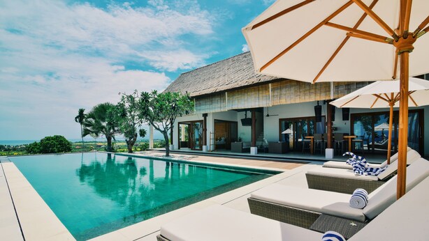 A poolside area with lounge chairs and umbrellas, a clear sky, and a view of the ocean. - Villa Banyan (Seririt)