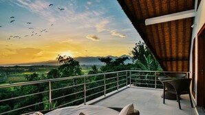A balcony with wicker furniture, a view of a sunset over a landscape, and a railing. - Villa Banyan (Seririt)