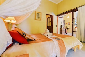A room with a bed, a nightstand, a lamp, and a door leading to another room.