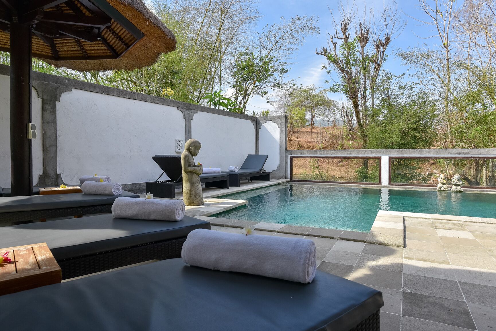 Zona de piscina con sillas de descanso, toallas y una estatua.