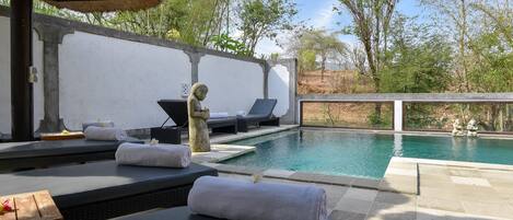 Zona de piscina con sillas de descanso, toallas y una estatua.
