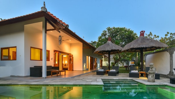 Une villa moderne dotée d’une piscine, d’un espace salon extérieur et de parasols en chaume.