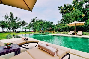 A poolside area with lounge chairs, a table with a plant, and an umbrella. - Villa Mahkai (Seririt)