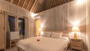 A hotel room with a large bed, wooden panel walls, a ceiling fan, and a minibar. - Villa Lumbung (Sukasada)