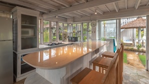 A kitchen with a large island, wooden cabinets, and a view of the garden. - Villa Lumbung (Sukasada)