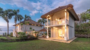 A two-story house with a thatched roof, a balcony, and a well-maintained garden. - Villa Lumbung (Sukasada)