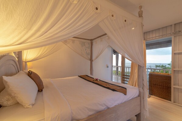 Un dormitorio con cama con dosel, vistas al mar y un balcón con mobiliario de mimbre.