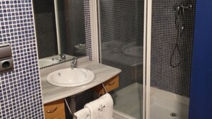 Un baño con lavamanos blanco, un espejo, una toalla colgada en un perchero y zona de ducha.